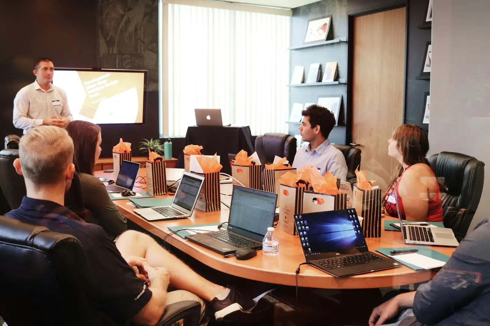 Presenter leading a workshop for a group seated around a table with laptops