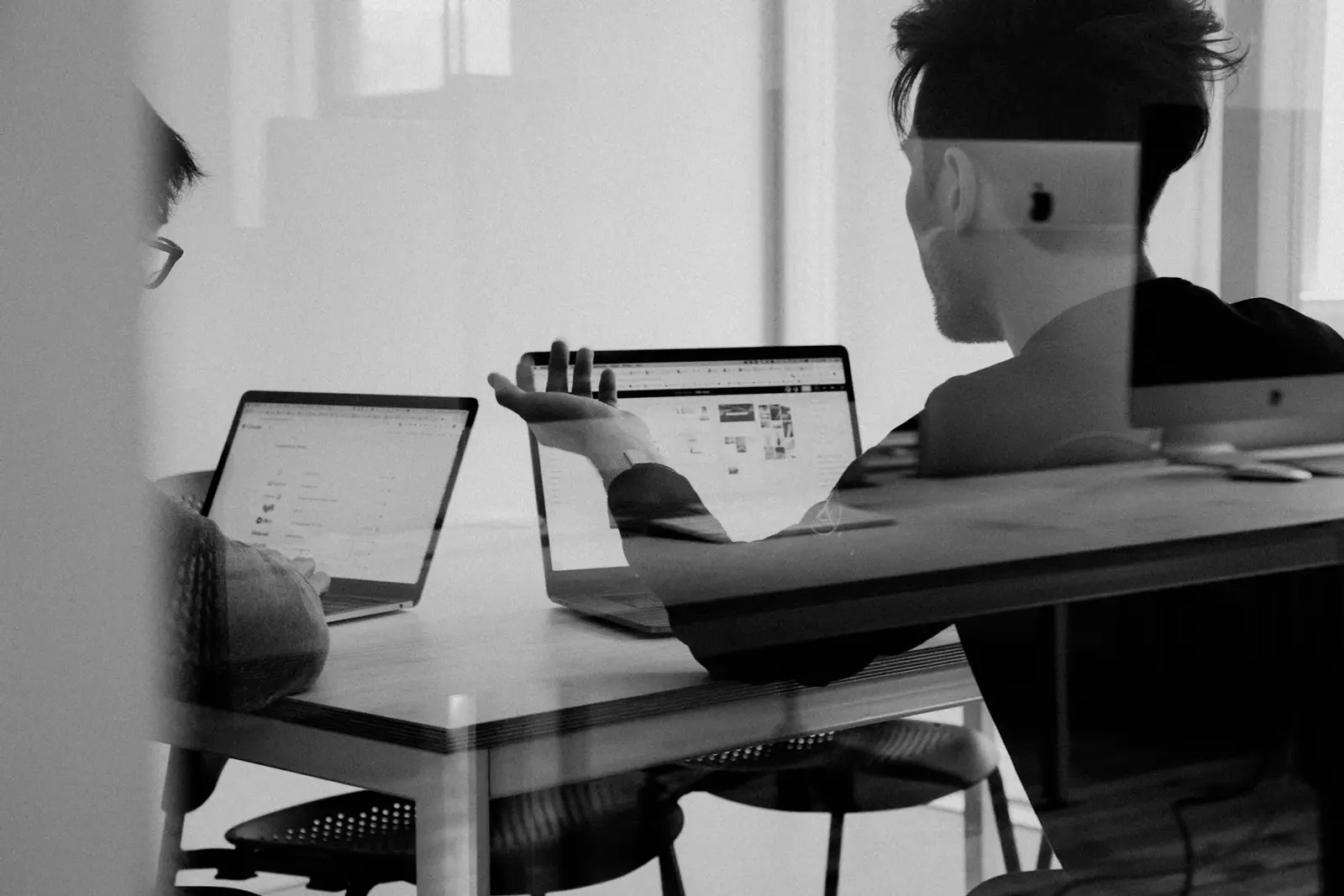 Black and white photo of a person working on a laptop at a desk in a bright room