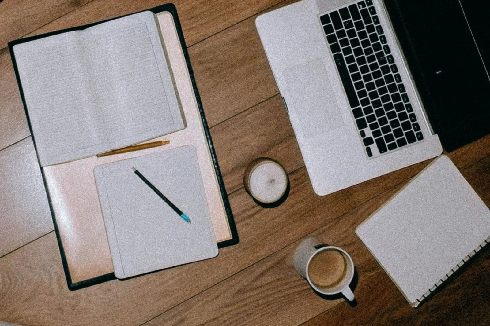 Overhead view of open notebooks, coffee cups and a laptop on a wooden table