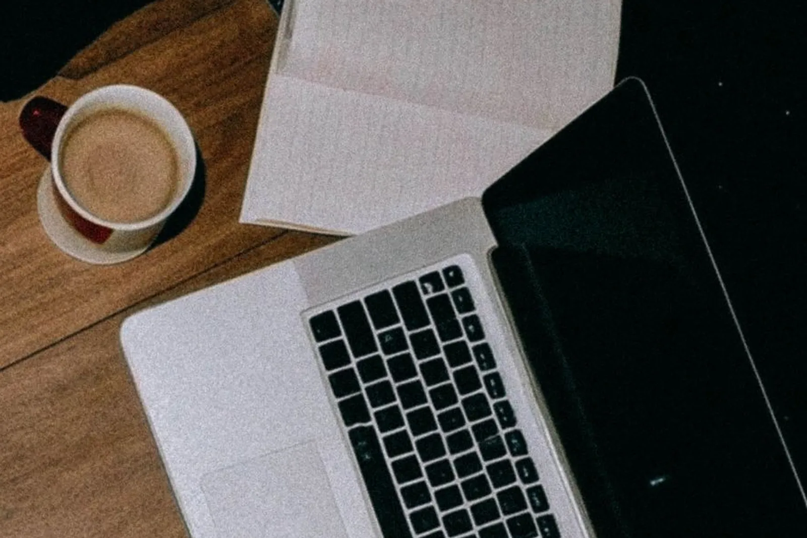Open laptop with notebooks and coffee on a wooden desk